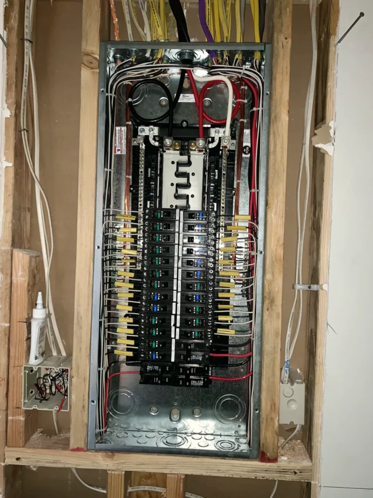 An open electrical panel with multiple circuit breakers and colored wires neatly organized inside a wooden frame enclosure.