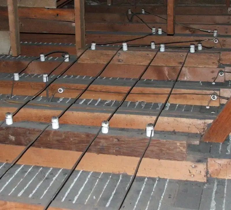 Image of an attic with old knob-and-tube electrical wiring mounted on wooden beams, showing the dated electrical system setup.