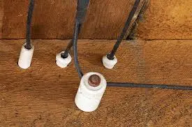 Old electrical wiring setup with four ceramic insulators and wires attached to a wooden surface.